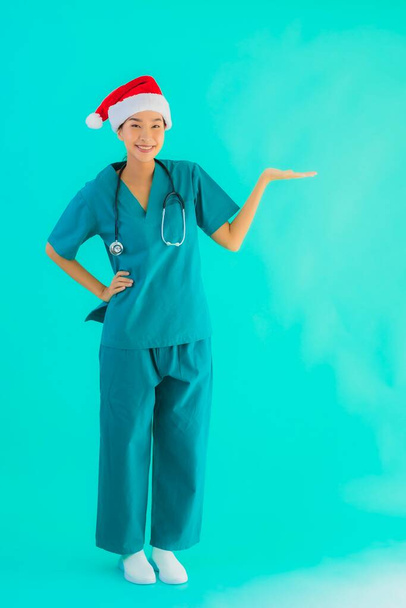Güzel bir Asyalı genç doktor portresi. Gülümsemeli bir Noel şapkası takıyor. Mavi izole arka planda mutlu. - Fotoğraf, Görsel