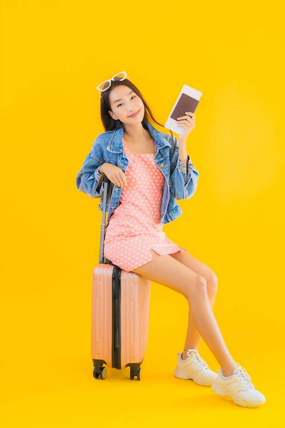 Πορτρέτο όμορφη νεαρή Ασιάτισσα γυναίκα με αποσκευές ταξιδιωτική τσάντα με διαβατήριο και κάρτα επιβίβασης σε κίτρινο απομονωμένο φόντο - Φωτογραφία, εικόνα