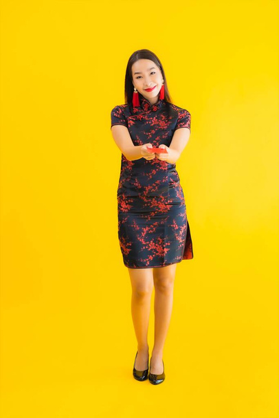 Porträt schöne junge asiatische Frau tragen chinesisches Kleid mit Ang Pao oder roten Buchstaben mit Bargeld für chinesische Neujahrskonzept auf gelbem Hintergrund isoliert - Foto, Bild