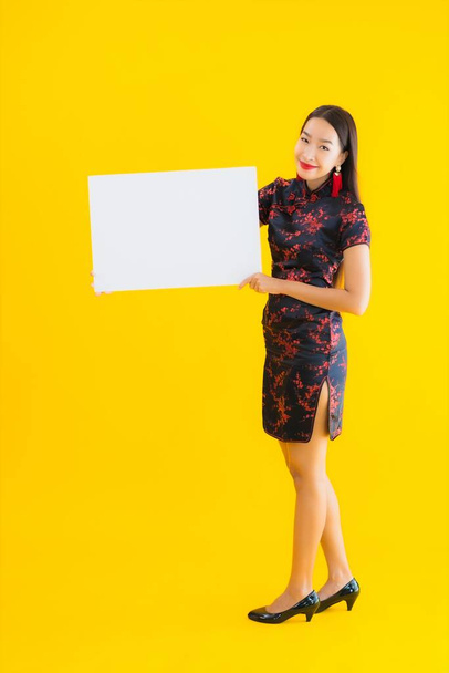 Портрет красивая молодая азиатская женщина носить китайское платье показать белый пустой рекламный щит для текста в китайском новый год концепции на желтом изолированном фоне
 - Фото, изображение