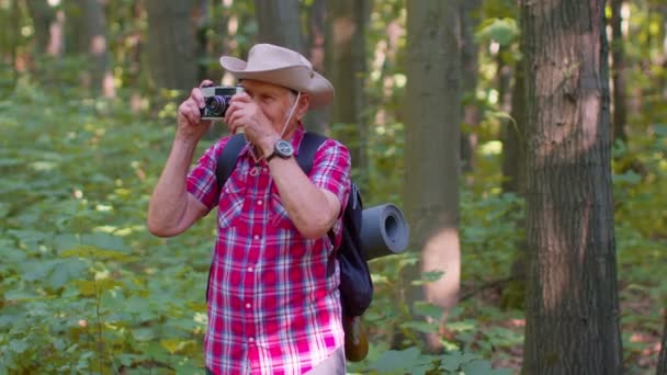 Senior-Mann-Großvater auf Wandertour mit Retro-Kamera im Wald unterwegs - Filmmaterial, Video