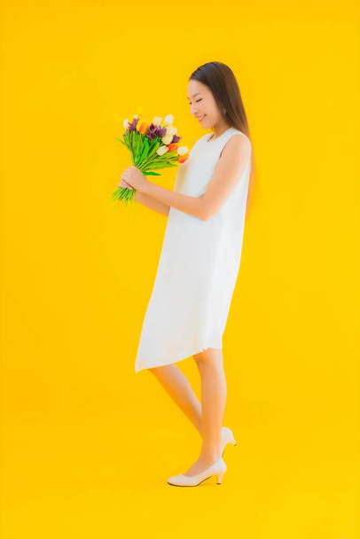 Retrato hermosa joven asiática mujer con flor en amarillo aislado fondo - Foto, imagen