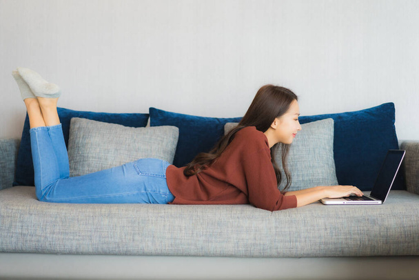 Retrato bonito jovem asiático mulher usar computador portátil no sofá na sala de estar interior - Foto, Imagem