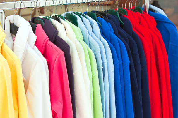 Разноцветные футболки из текстиля, висящие в магазине
 - Фото, изображение