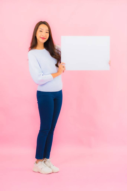 Портрет красива молода азіатка показує порожній білий рекламний щит для тексту на фоні рожевого кольору
 - Фото, зображення