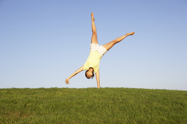Young woman cartwheels in field - 写真・画像