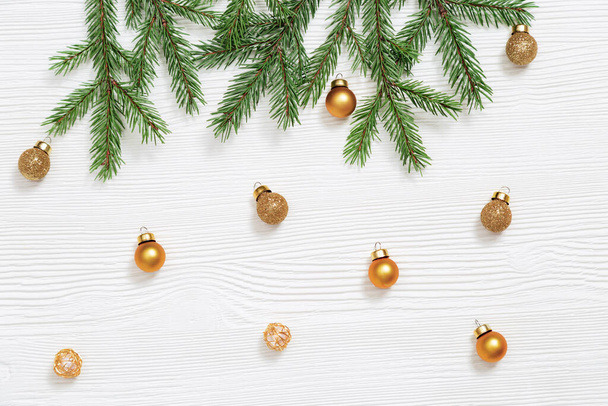 Metallic golden toys fall, small bright balls, natural green fir tree branches on white wooden table. Winter Holiday concept. Flat lay. Top view. - Photo, image