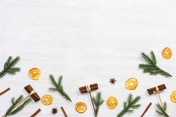 Winter or Christmas fragrance, spices, cinnamon, dry orange slices, anise star, pine branches on white wooden background with copy space. Flat lay, top view. - Foto, imagen