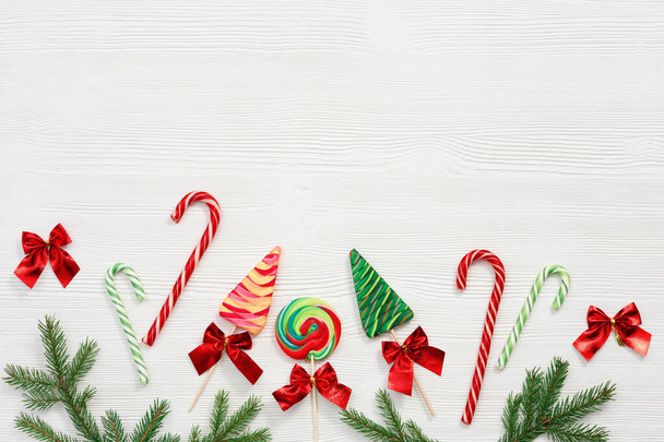 Christmas sweets assorted top view, green fir branches, wooden toys on white background, flat lay. Bright New Year candy and lollipops. - Foto, imagen