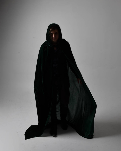 Full length portrait of a  brunette man wearing black shirt, waistcoat and a green velvet cloak.  Standing  action pose isolated  against a grey studio background. - Фото, зображення