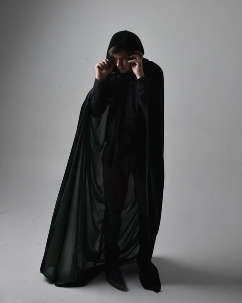 Portrait complet d'un homme brune portant une chemise noire, un gilet et un manteau de velours vert. L'action debout pose isolée sur un fond de studio gris. - Photo, image