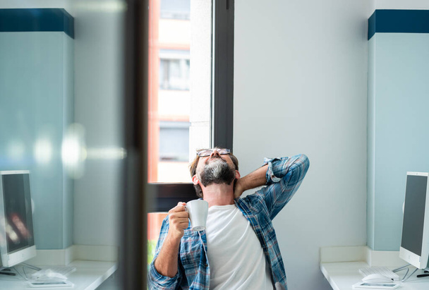 Erwachsener Mann berührt seinen Nacken und Rücken wegen Stressschmerzen und Krankheiten, die durch Arbeitshaltung verursacht werden  - Foto, Bild