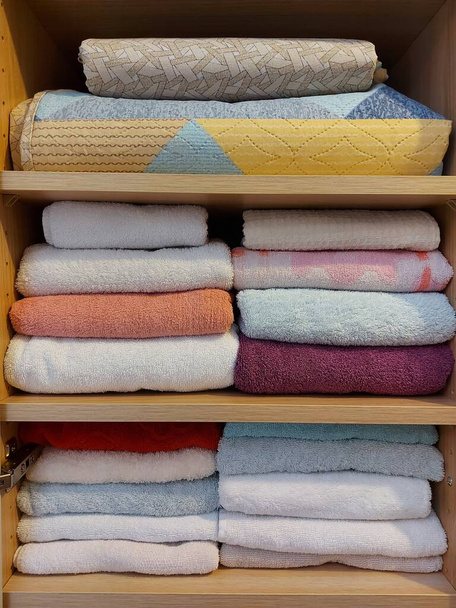 Wielokolorowe bawełniane ręczniki frotte ułożone starannie na półkach w szafie. Strona główna włókiennicze tło - Zdjęcie, obraz