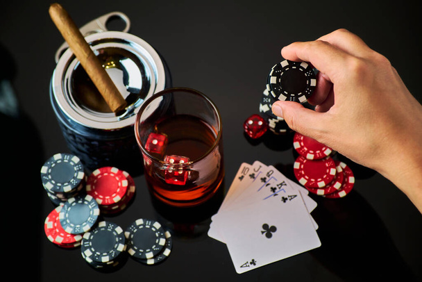 Чипсы казино, игральные карты, стакан виски и кубики на темном отражающем фоне - Фото, изображение