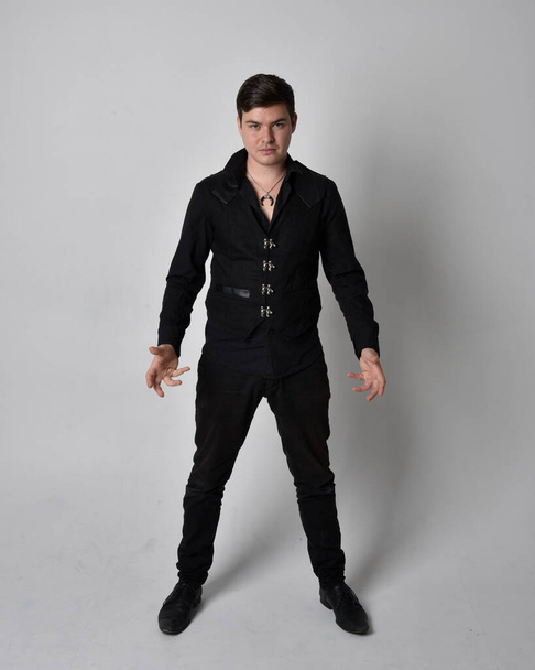 Retrato de comprimento total de um homem morena vestindo camisa preta e colete gótico. pose de pé isolado contra um fundo estúdio cinza. - Foto, Imagem
