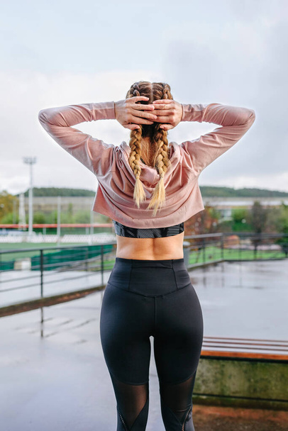 Молодая спортсменка растягивает шею и плечи на открытом воздухе - Фото, изображение