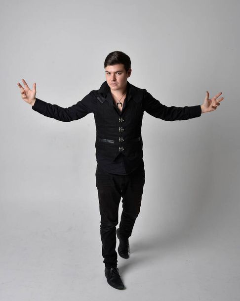 Full length portrait of a brunette man wearing black shirt and gothic waistcoat.  Standing pose isolated  against a grey studio background. - Fotoğraf, Görsel
