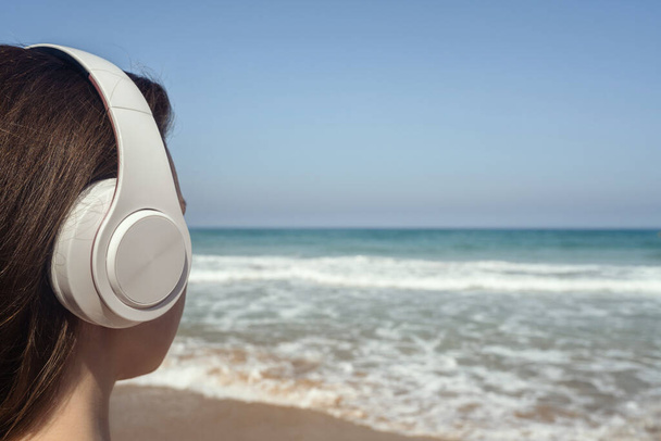 Back view of alone woman sitting on a beach in headphones listen music dreaming and looking on the sea. Female relaxation at summer vacation. - Fotoğraf, Görsel