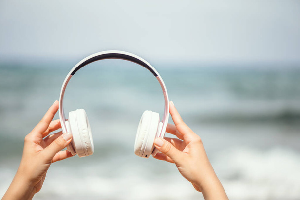 Woman hands with headphones on a beach and sea coastline. - Foto, Imagen