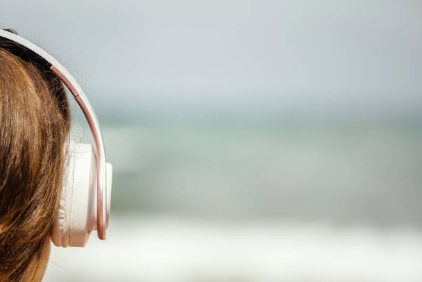 Visszapillantás a magányos nő ül a strandon a fejhallgató zenét hallgatni álmodik, és nézi a tengert. Női kikapcsolódás a nyári szünetben. - Fotó, kép