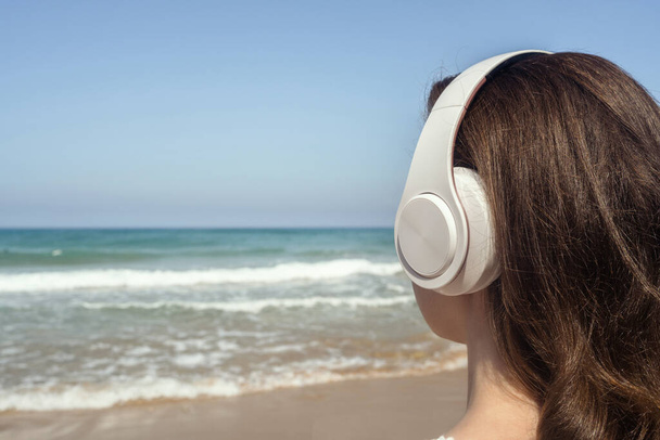 Alone woman on a beach in headphones listen music looking on the sea. Female relaxation at summer vacation. Back view - Foto, immagini