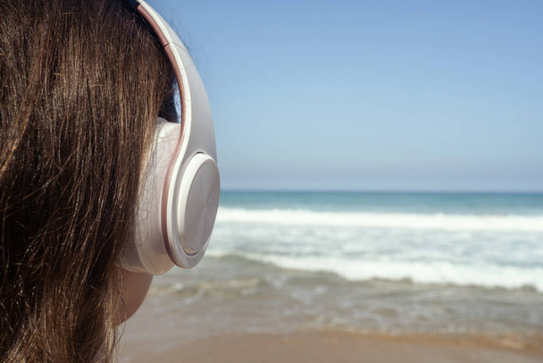 Alone woman on a beach in headphones listen music looking on the sea. Female relaxation at summer vacation. Back view - Fotó, kép