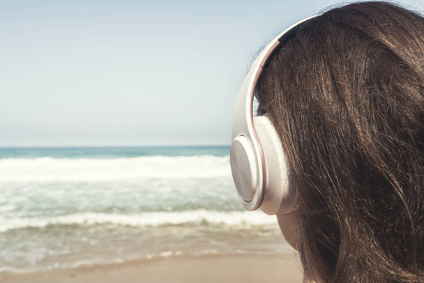 Alone woman on a beach in headphones listen music looking on the sea. Female relaxation at summer vacation. Back view - Foto, Bild