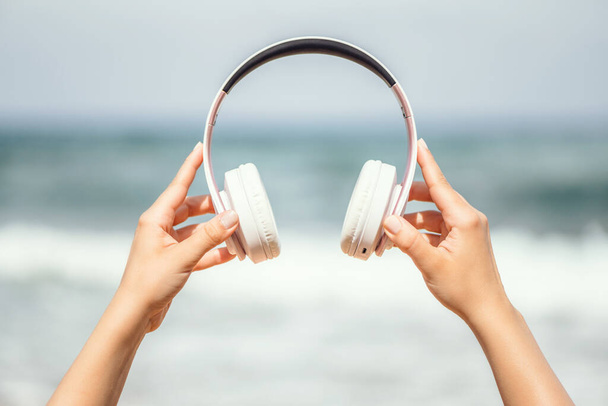 Woman hands with headphones on a beach and sea coastline. - Фото, зображення
