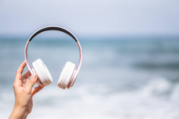 Woman hands with headphones on a beach and sea coastline. - Fotoğraf, Görsel