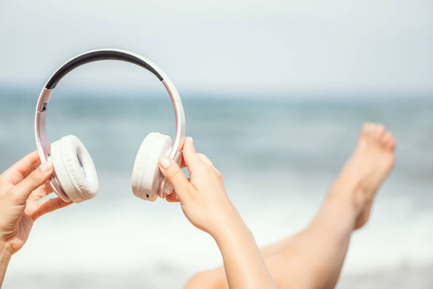 Woman hands with headphones on a beach and sea coastline. - Fotoğraf, Görsel