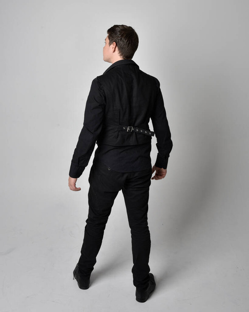 Retrato de comprimento total de um homem morena vestindo camisa preta e colete gótico. pose de pé isolado contra um fundo estúdio cinza. - Foto, Imagem