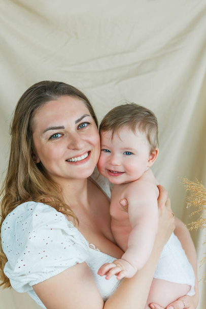 Beautiful young mother with blue-eyed little daughter on a beige background. - Photo, Image