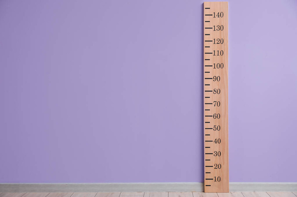Велика лінійка для вимірювання висоти біля кольорової стіни
 - Фото, зображення