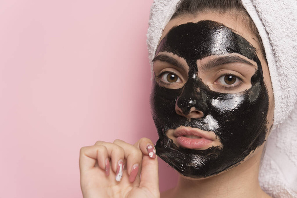 mujer joven con mascarilla facial en la cara aplicando crema cosmética en la cabeza - Foto, Imagen