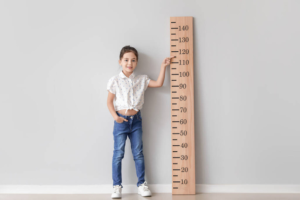 Little girl measuring height near light wall - Φωτογραφία, εικόνα