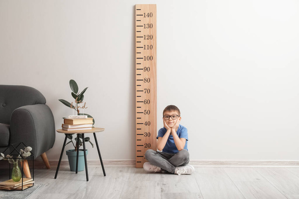 Little boy sitting near big ruler for measuring height at home - 写真・画像