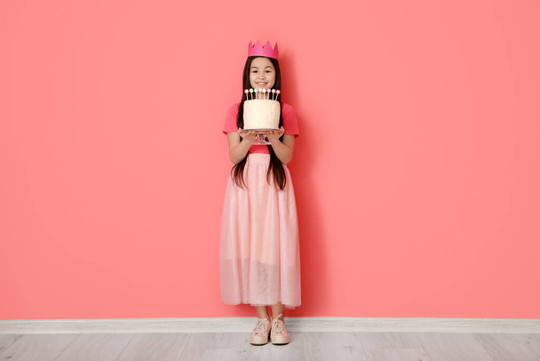 Nettes kleines Mädchen mit Geburtstagstorte auf farbigem Hintergrund - Foto, Bild
