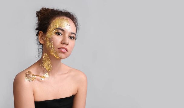 Beautiful young African-American woman with golden paint on her body against grey background - Photo, Image
