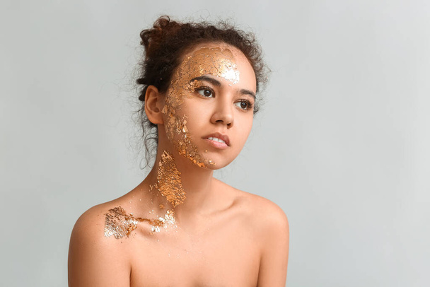 Krásná mladá afroamerická žena se zlatou barvou na jejím těle proti šedému pozadí - Fotografie, Obrázek