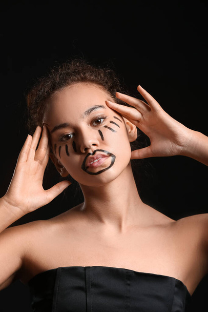 Beautiful young African-American woman with paint on her face against dark background - Фото, изображение