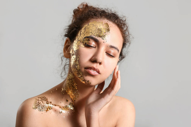 Beautiful young African-American woman with golden paint on her body against grey background - 写真・画像