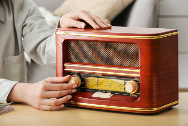 Woman with retro radio receiver on table in room, closeup - 写真・画像