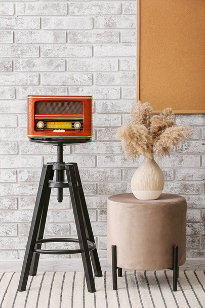 Retro radio receiver on table and pouf with vase near brick wall - Fotó, kép