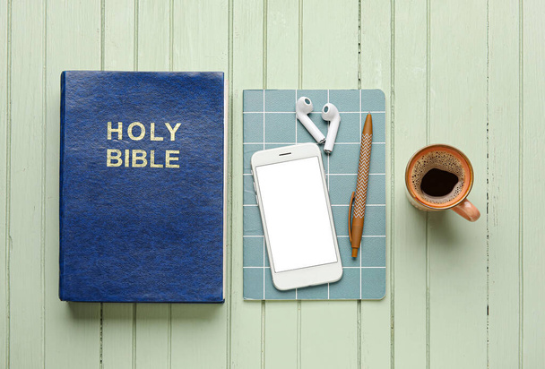 Holy Bible, cup of coffee, mobile phone and earphones on color wooden background - Foto, imagen