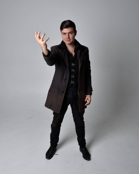 Retrato de comprimento total de um homem morena usando casaco de couro preto. pose de pé isolado contra um fundo estúdio cinza. - Foto, Imagem