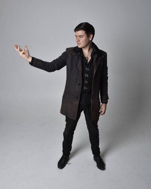 Full length portrait of a brunette man wearing black leather coat.  Standing pose  isolated  against a grey studio background. - Foto, immagini