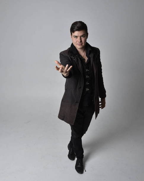 Full length portrait of a brunette man wearing black leather coat.  Standing pose  isolated  against a grey studio background. - Photo, Image