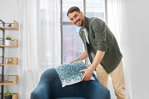happy smiling man arranging chair cushion at home - Photo, Image