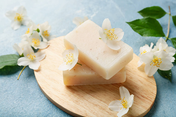 Board with soap bars and jasmine flowers on color background - 写真・画像