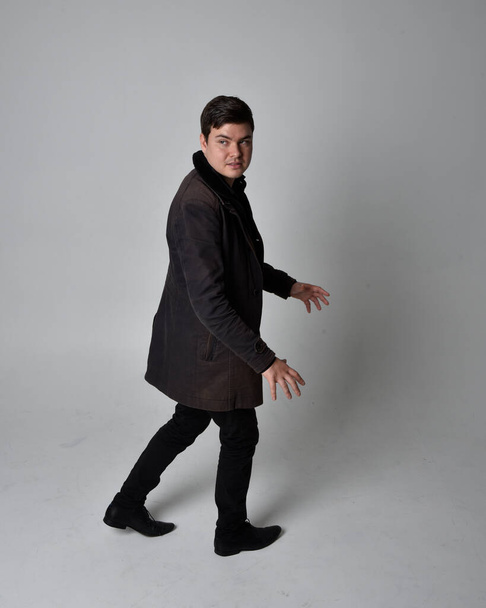 Full length portrait of a brunette man wearing black leather coat.  Standing pose  isolated  against a grey studio background. - Fotoğraf, Görsel